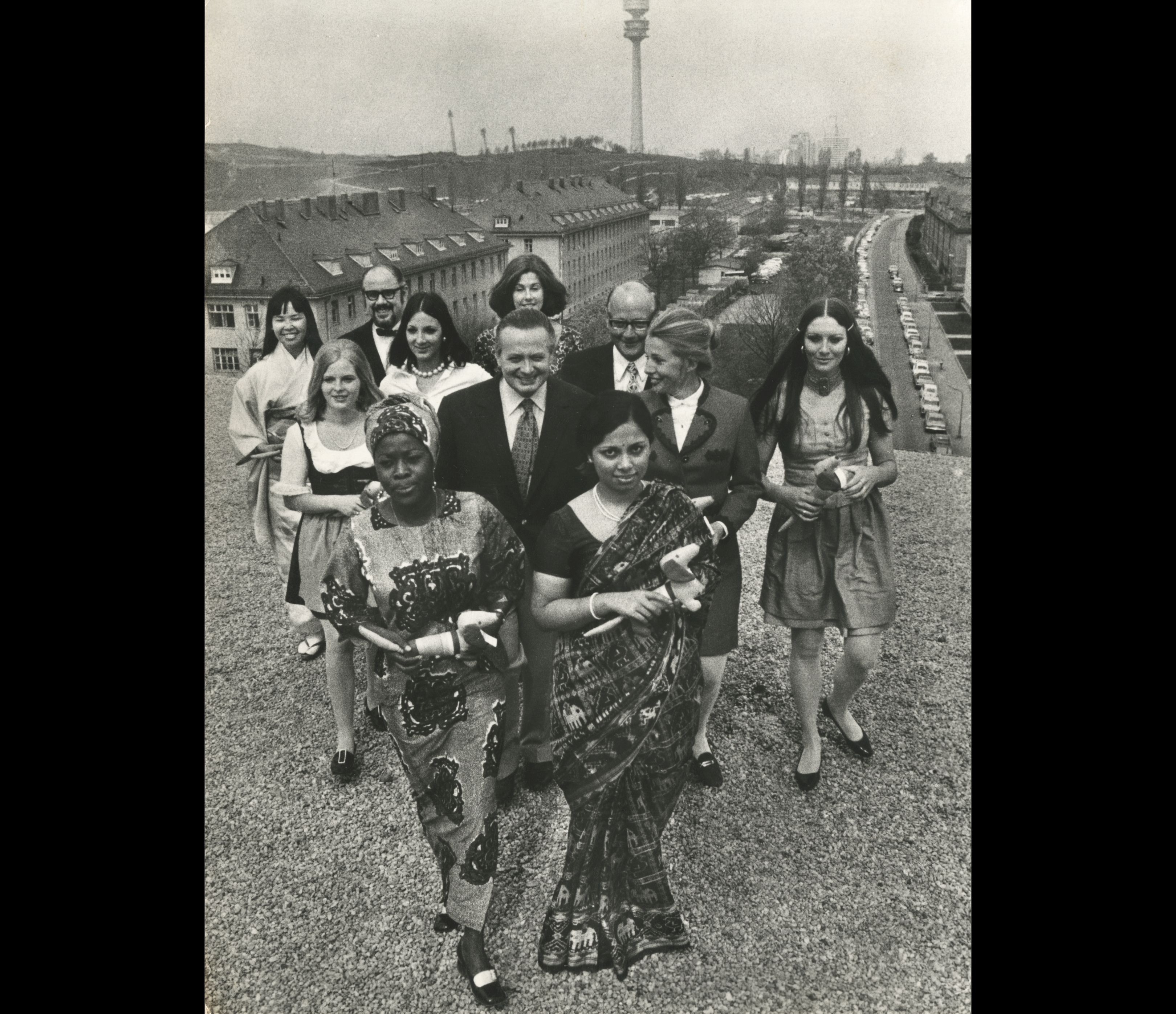 Provenientes do Gana, da Índia, do Japão, do Brasil e de Munique apresentam-se aqui as oito primeiras "Olympia-hostenssen" (recepcionistas) em companhia do presidente do Comitê Organizador da XX Olímpiada de Munique 1972, Sr. Willi Daume ( ao centro).